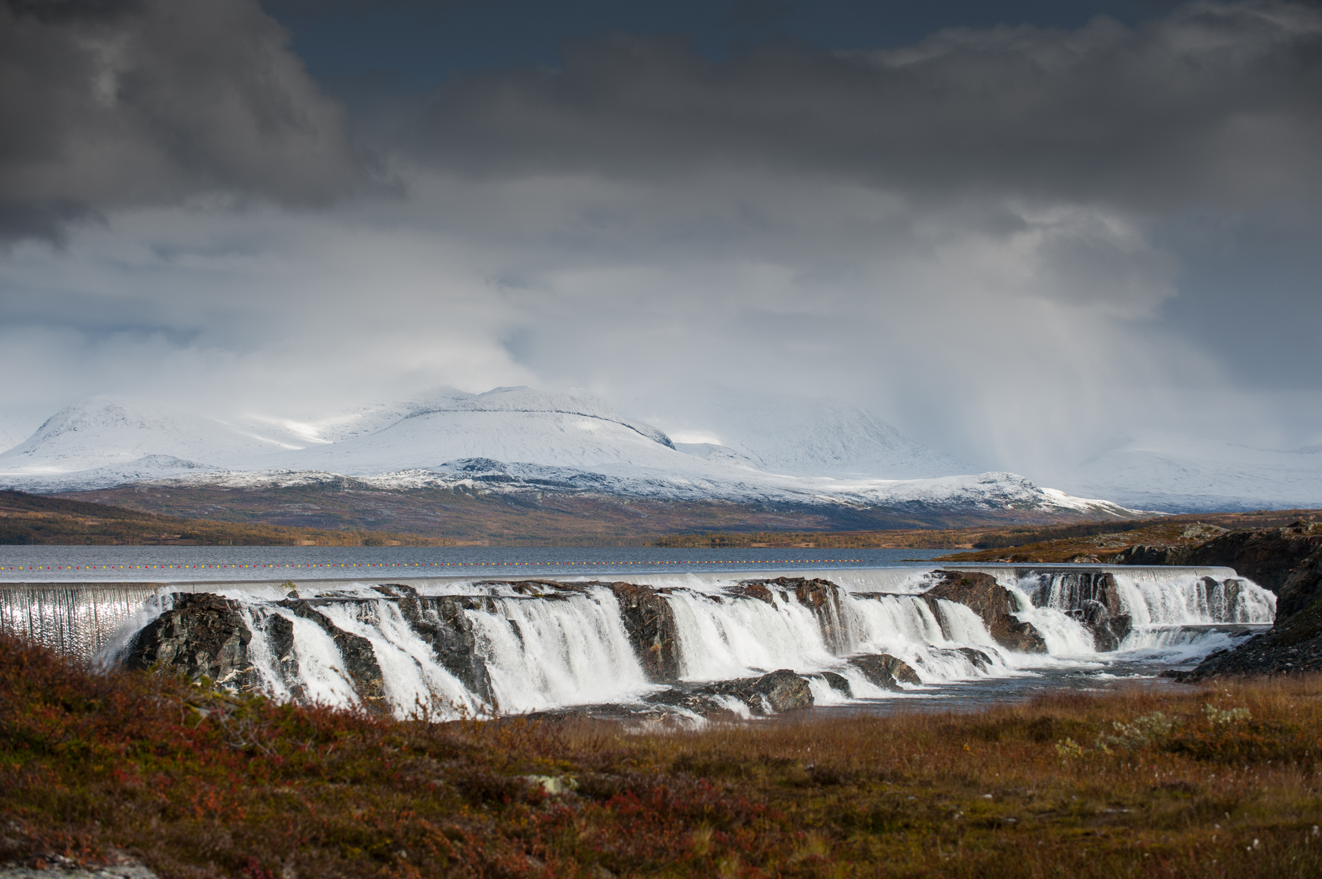 Uma foto da paisagem mostra a barragem de Nesjo com montanhas com neve ao fundo