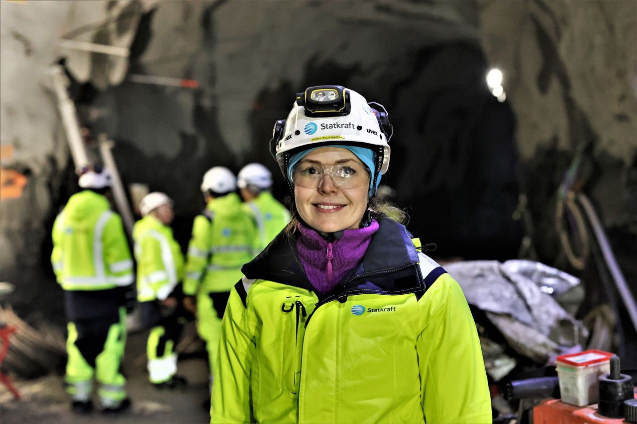 Uma mulher trajada com EPIs e uniforme da Statkraft. Em segundo plano, um grupo de pessoas.