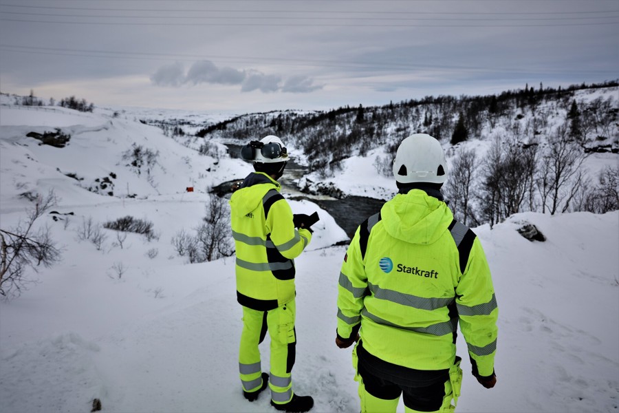 Duas pessoas vestem o uniforme da Statkraft e estão em pé de costas em um ambiente externo nevado